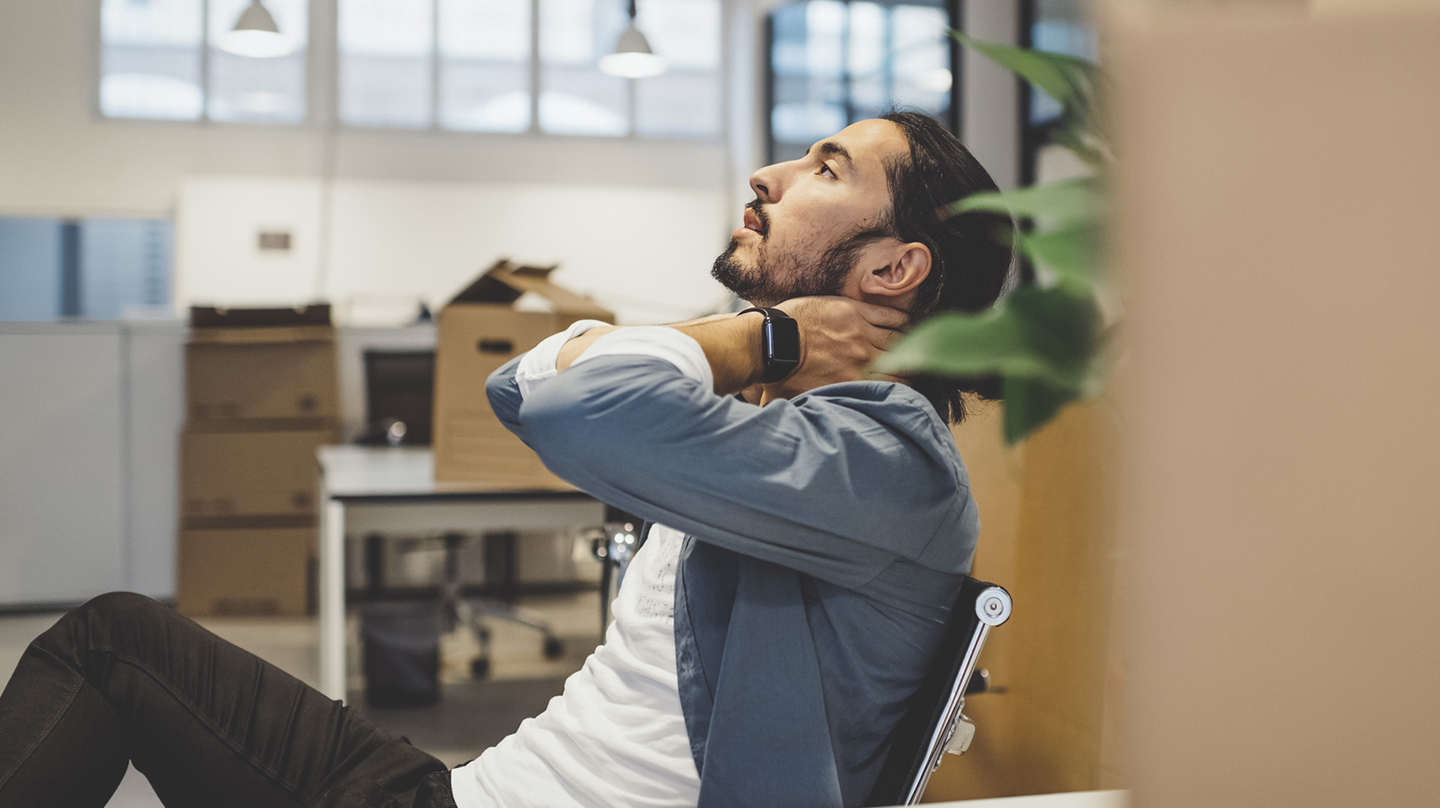 Ein junger Mann sitzt auf einem Bürostuhl und hält sich den schmerzenden Nacken.